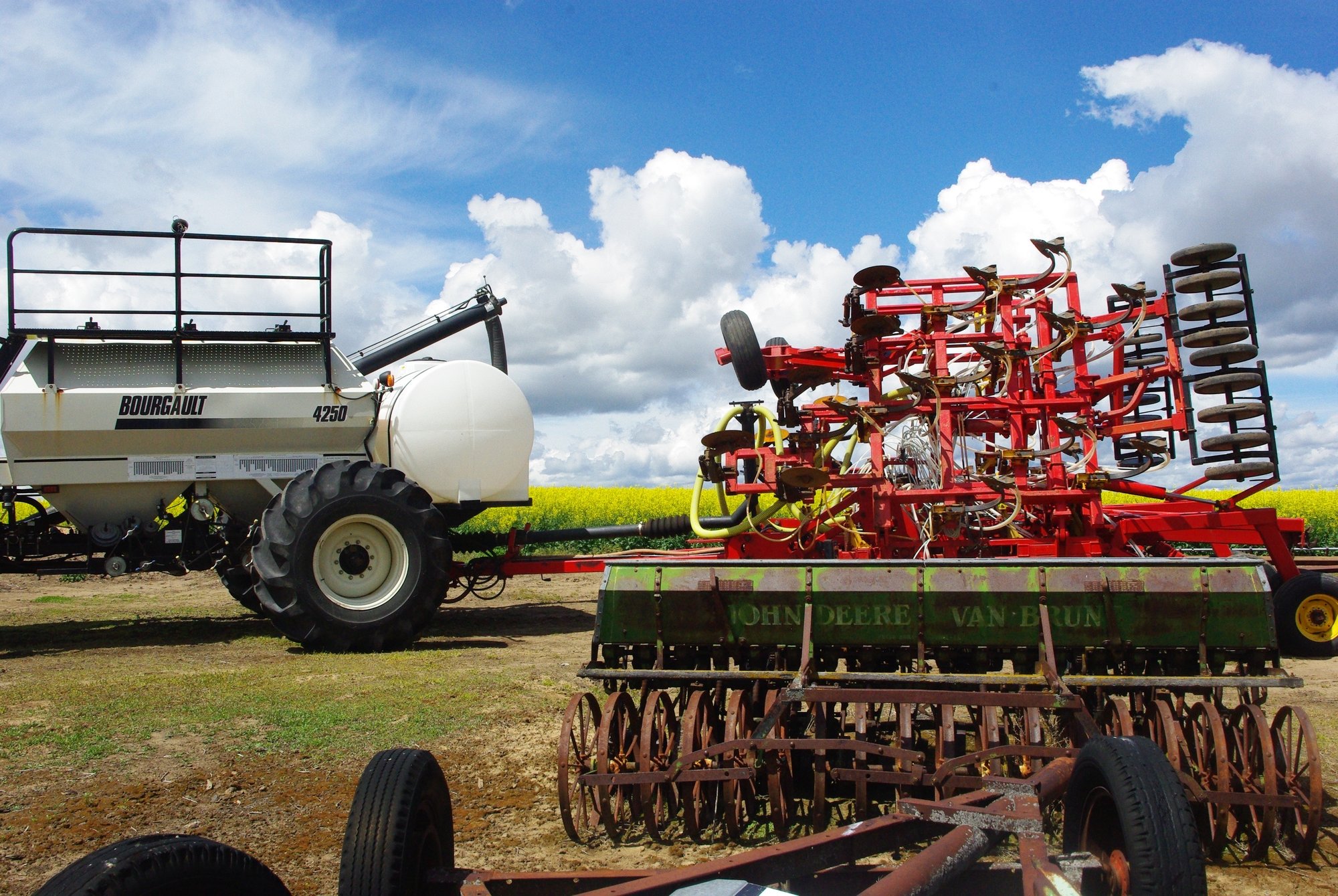Large agricultural seeding equipment parked beside a flowering field