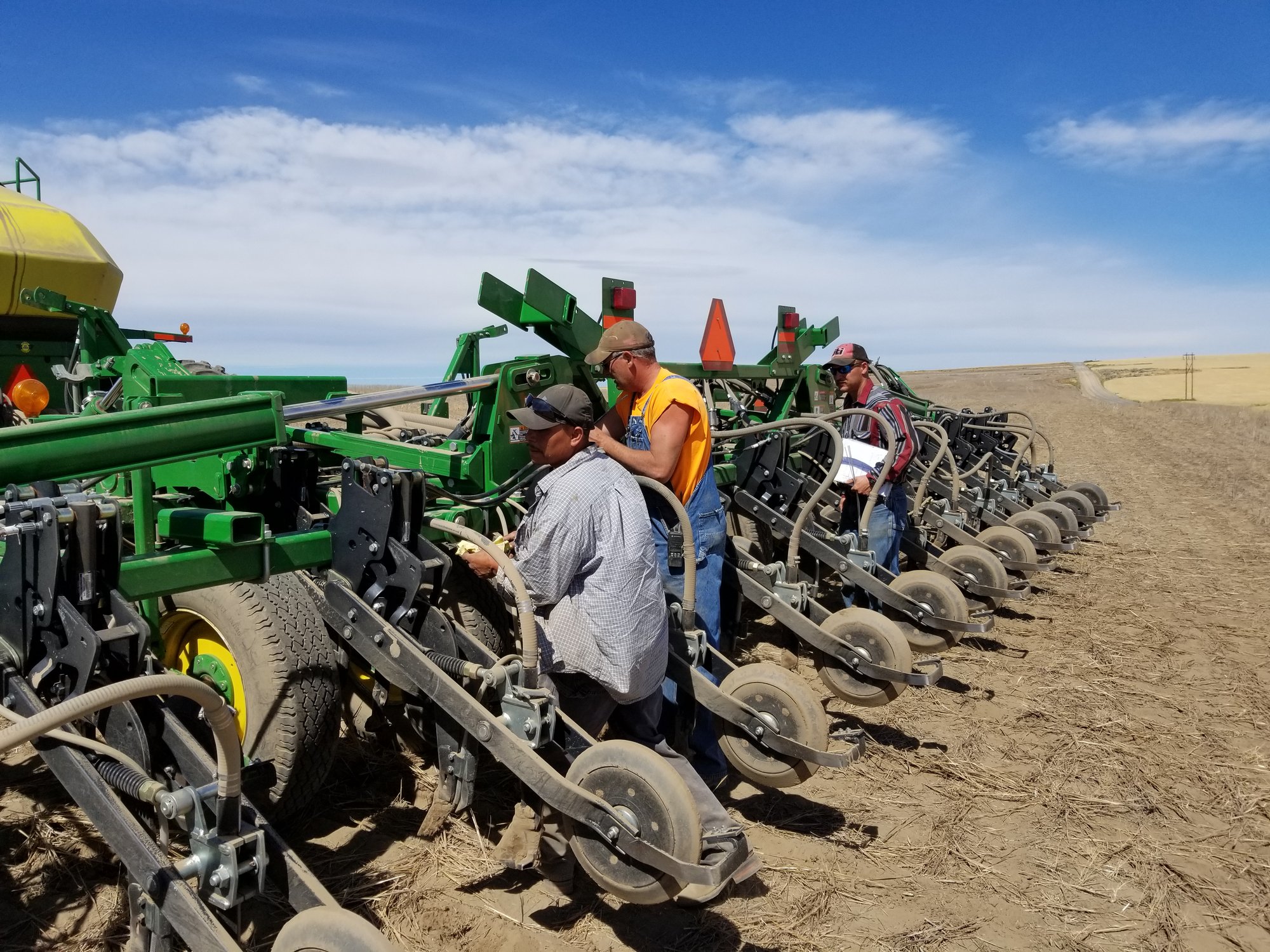 Farmers inspect planting equipment in a dry field