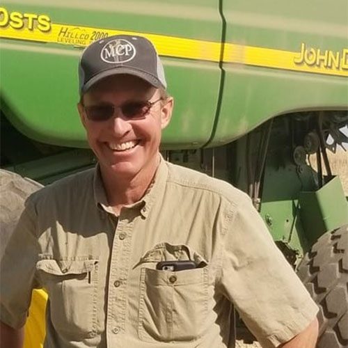 Smiling farmer standing beside green John Deere machinery