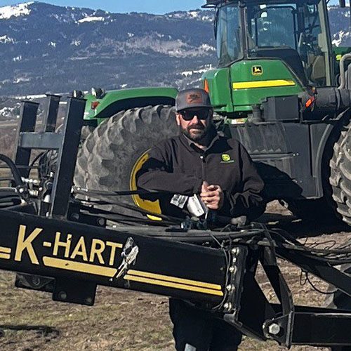 Farmer standing beside John Deere tractor and K-Hart equipment