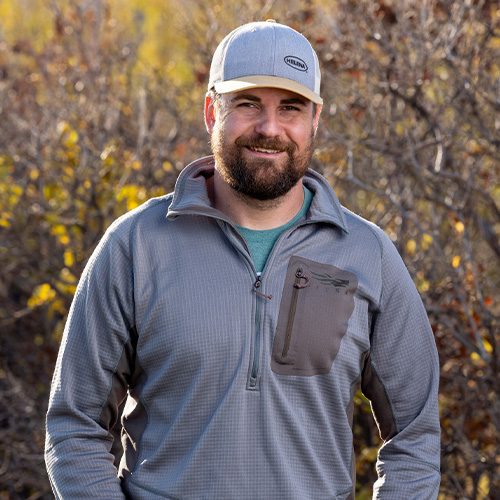 Smiling bearded man outdoors wearing cap and gray pullover
